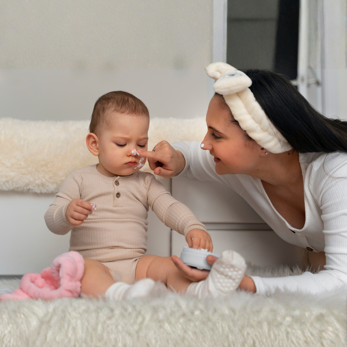 Woman applying cream to a baby's face in a cozy indoor setting